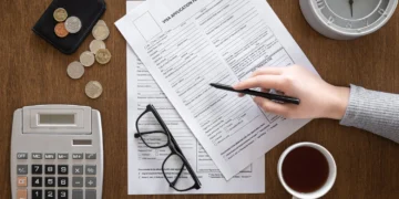 meja diatasnya terletak kopi, uang, kalkulator, dan tangan sedang menghitung keuntungan investasi di SBR014