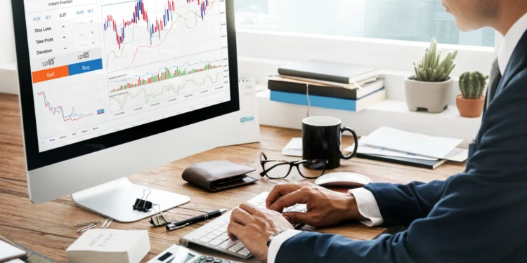 Seorang pria memakai jas sedang duduk di depan komputer menganalisis Sucorinvest Money Market Fund